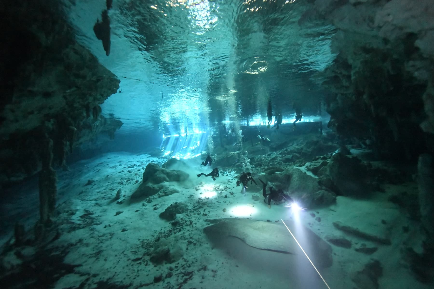 Divers in a cenote cavern lit by beams of light from the surface