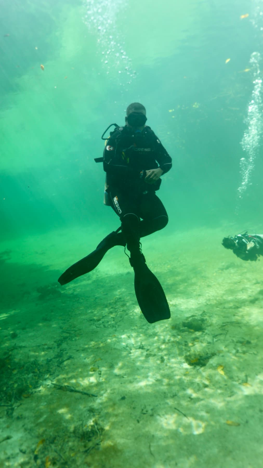 A diver hovering above a sandy cenote floor
